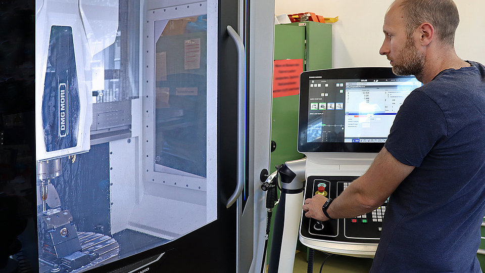 Photo of a male technician operating a 5-axis milling machine.