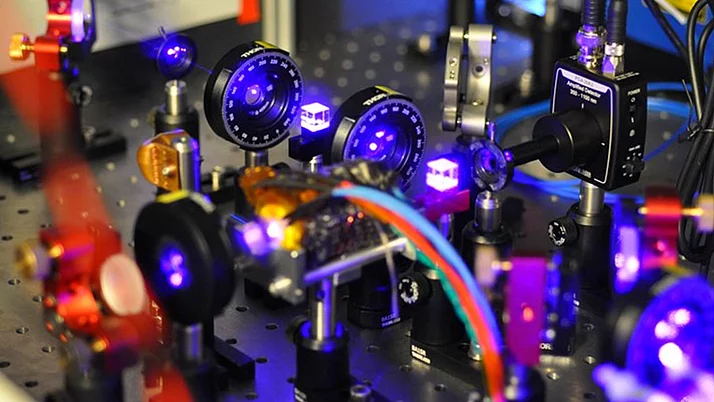 Komplexe Anordnung von optischen Geräten auf einer Laborplatte. Mehrere Linsen und Kameras sind in unterschiedlichen Positionen angeordnet, die mit bunten Kabeln verbunden sind.