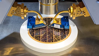 Das Bild zeigt eine hochpräzise Messapparatur, die zwei goldene Probenaufnahmegeräte über einer CPU-Wafer-Plattform platziert. Die Wafer-Oberfläche ist mit komplexen, strukturierten Mustern bedeckt, die in der Halbleiterfertigung verwendet werden.