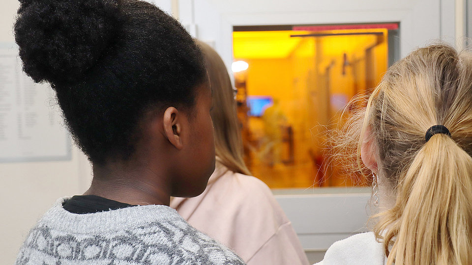 Photo showing 3 girls looking through a window into a clean room. 