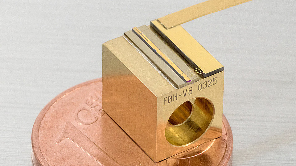 Photo of a mECDL chip mounted on a C-mount. The mECDL chip is a small, rectangular device with a metallic gold color. It is placed on top of a 1 Euro cent coin, illustrating its compact size. 