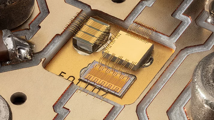 Close-up of an electronic circuit with gold and silver components. You can see several microscopically small components on a circuit board, connected by fine wires.