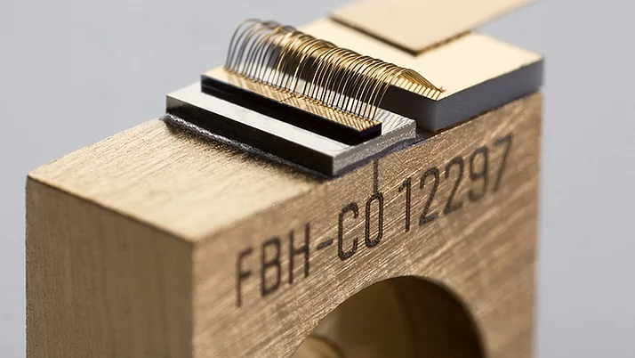 Close-up of a gold-colored electro-optical component. At the top is an arrangement of fine wires on a black base mounted on a rectangular block.