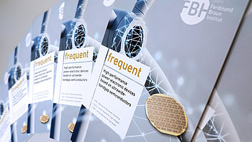 The picture shows several issues of the FBH publication frequent on wide-gap semiconductors. On the cover you can see the title, logo and a wind turbine as well as 3 wafers arranged around the title.