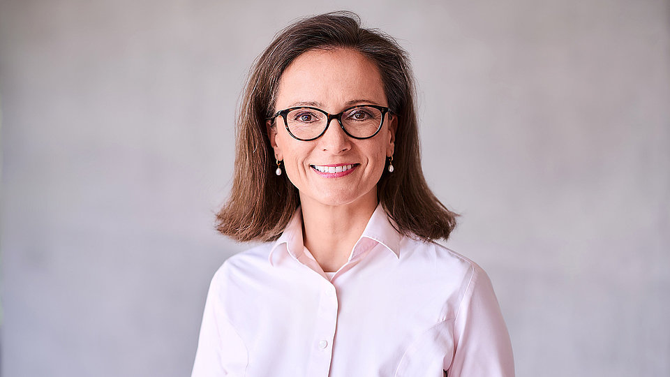 The photo shows Karin-Irene Eiermann, administrative managing director of FBH, standing in front of a gray wall in a light-colored blouse.