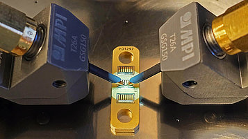 Close-up of a GaN HEMT device being tested using two MPI probe tips, highlighting precise measurement connections on a golden test fixture.