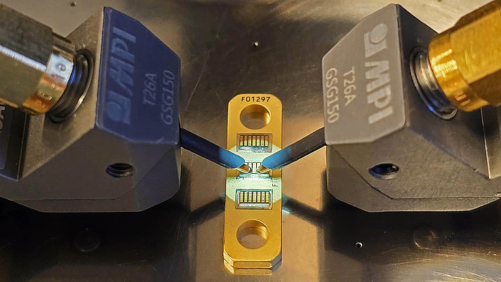 Close-up of a GaN HEMT device being tested using two MPI probe tips, highlighting precise measurement connections on a golden test fixture.