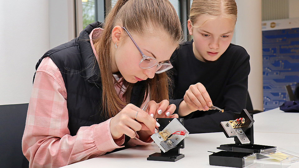 Photo of the 2 girls inserting FBH lasers with tweezers in a holder for measuring. 