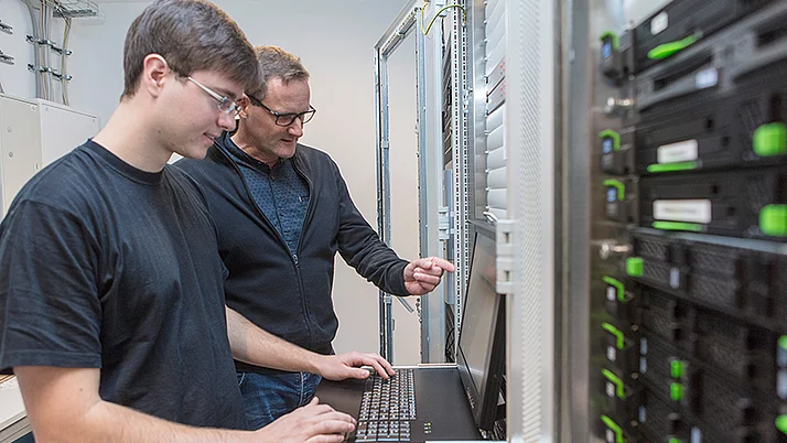 Two IT specialists standing in front of a computer in a server room.