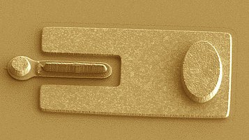 A close-up of a transistor featuring a metallic rectangular structure with a U-shaped cutout and an oval element, showcasing its microfabricated design.