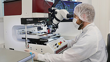 The photo shows a male technician in a lab coat using a pick-and-flip station.