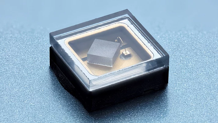 Microchip in a transparent housing. The chip has a square shape and is positioned on a gold-colored background.